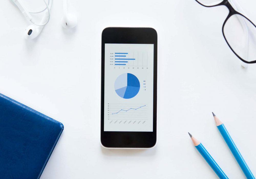 White office desk with glasses, mobile phone with a diagram, earphones and pencils on it. Male office supply. Top view, business concept photo